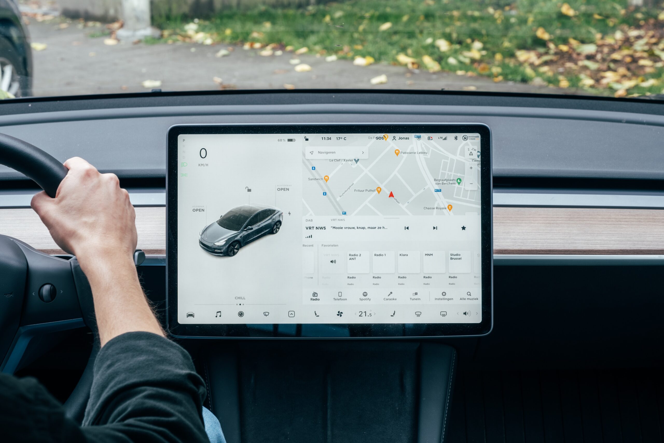 Driver's hand on the steering wheel of a car with a touchscreen navigation display